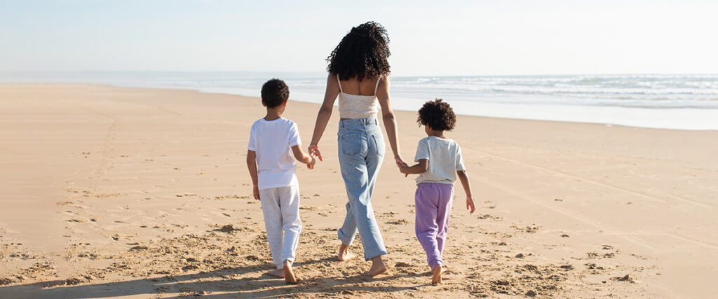 Back view of mother and children holding hands on beach