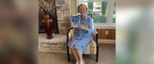 Lisa Graff's in living room holding up her book “Up in the Sky So Blue"